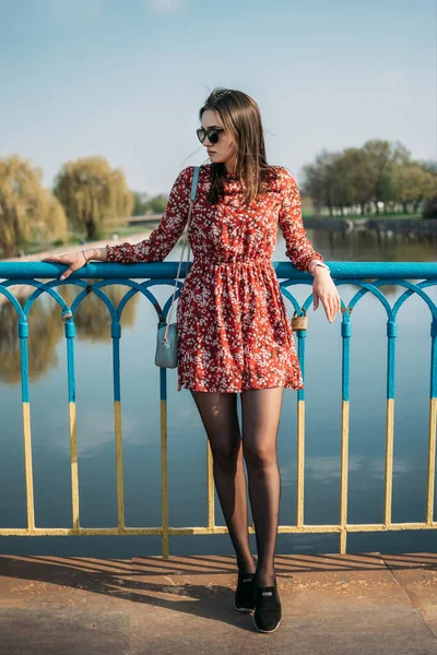 Spring fashion trend, outfit, comfort city look. Outdoor portrait of young happy smiling brunette woman wearing red flower dress and walking in street of European city