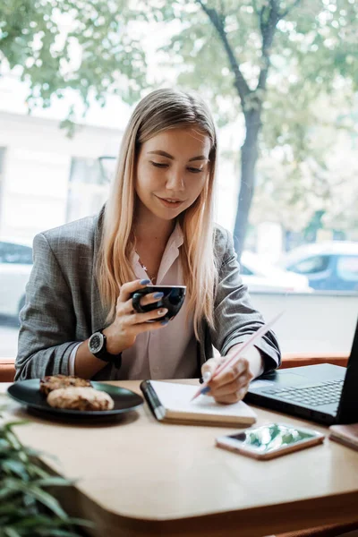 Young girl student sitting in cafe with laptop, smartphone and cup of coffee. Student learning online, distant education, remote freelancer working in coffee shop