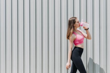 Spor ve hidrasyon, su içmek, egzersiz sırasında susuz kalmak. Spor yapan genç bir kadın, genç bir kız yaz günü açık havada koştuktan sonra su içiyor.