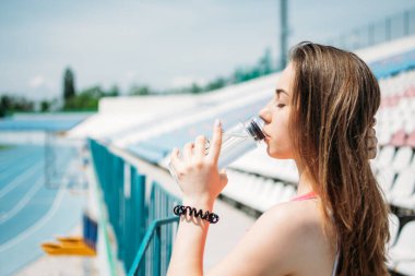 Spor ve hidrasyon, su içmek, egzersiz sırasında susuz kalmak. Spor yapan genç bir kadın, genç bir kız yaz günü açık havada koştuktan sonra su içiyor.