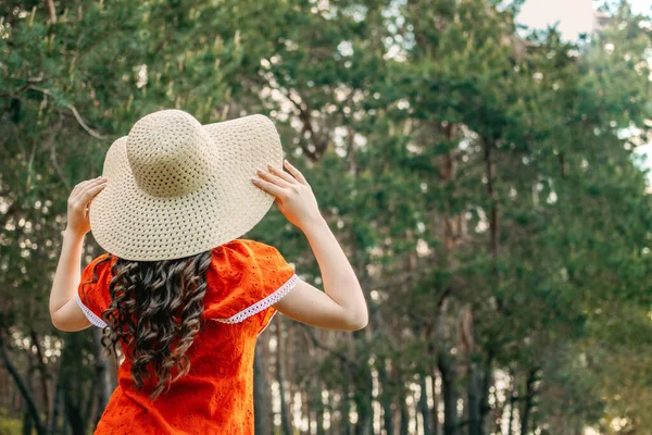 Enjoying the nature, wellness, wellbeing, healthy lifestyle, slow living. Young brunette girl in red dress and straw hat walking in forest, woods.