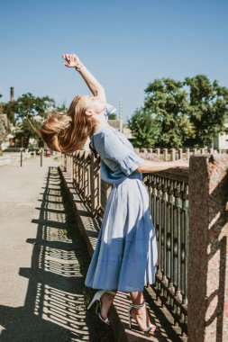 Yazı şehirde geçirmek, sıcağa dayanmak, yaz kıyafetleri, solunabilir kumaşlar. Şehir caddesinde mavi keten elbiseli genç sarışın kadın.