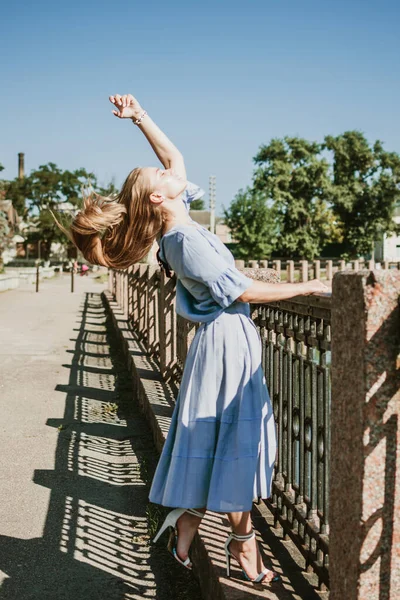 Yazı şehirde geçirmek, sıcağa dayanmak, yaz kıyafetleri, solunabilir kumaşlar. Şehir caddesinde mavi keten elbiseli genç sarışın kadın.