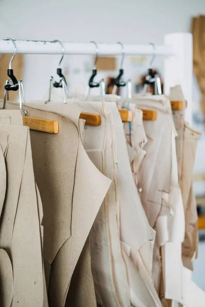 Muitos padrões de costura de papel para roupas diferentes penduradas no rack no fundo da fábrica de costura. Padrão de roupa, fabricação na fábrica de costura. Alfaiataria, pequenas empresas — Fotografia de Stock