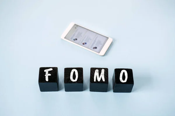 FOMO, Боязнь пропустить, социальная тревога, постоянная связь, страх сожаления, Социальная сеть. Текст FOMO с размытым мобильным телефоном и социальными сетями на синем фоне — стоковое фото