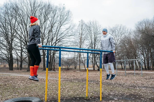 Outdoor Pull-up Bar and Parallel Bars workout. Socially distant bootcamps. Group fitness workout classes outdoors in public parks. Woman and man training together. Health, wellness and community