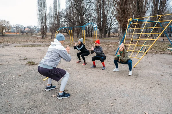 Grupowe zajęcia fitness na świeżym powietrzu. Odległe społecznie zajęcia na świeżym powietrzu w parkach publicznych. Trzy kobiety i mężczyźni trenują razem w parku publicznym. Zdrowie, wellness i koncepcja wspólnotowa — Zdjęcie stockowe