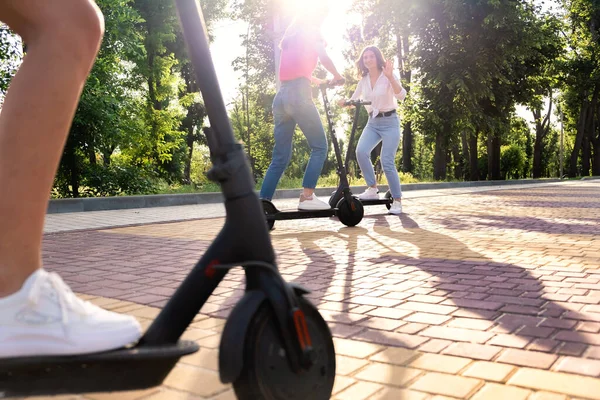 Sommeraktivitäten für Jugendliche und Erwachsene. Fahrrad- und Elektrorollerverleih. Summer Bucket List, lustige Ideen für Erwachsene. Junge Freundinnen fahren Elektroroller in der Stadt Straße, Park — Stockfoto