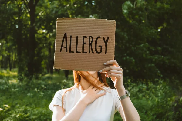 Mujer pelirroja joven cubre su cara con alergia al texto de signos. Retrato sin rostro de mujer con signo de alergia en el fondo de la naturaleza. Alergia al polen, alergia primavera verano —  Fotos de Stock