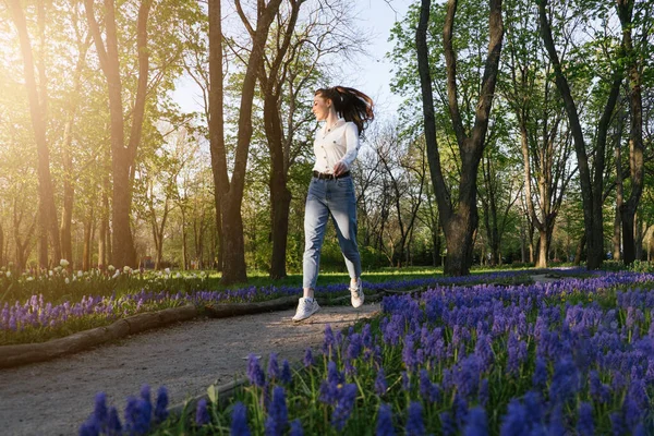 Enjoy every moment, Enjoying life, Positive emotions, Ways to Be Happier. Happy Young woman jumping and enjoying life at green park with flowers. — Stock Photo, Image