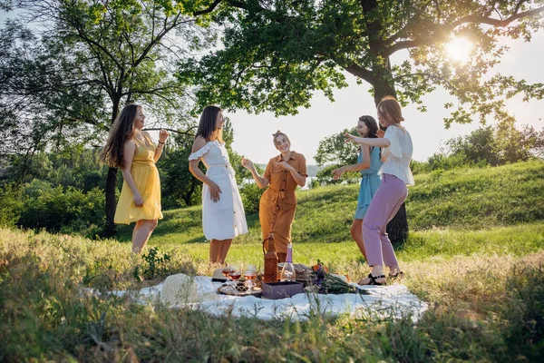 Summer party, Outdoor Gathering with friends. Five young women, Friends at the picnic dancing and having fun on summer vacation. Group of female friends enjoying at outdoors party on nature.