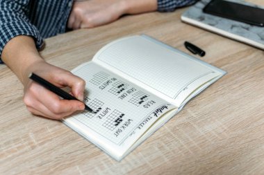 Bullet Journal, Habit Tracker. Female hand notes in habits tracker. Woman cross off day with routine in her Habit Tracker. Selective focus