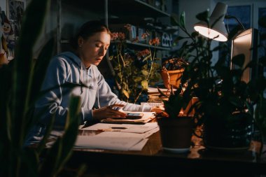 Küçük işletme sahibi, tasarımcı işyeri. Kadın tasarımcı, dikiş stüdyosu sahibi, yaratıcı stüdyo çalışanı akşamları bilgisayarla birlikte masaüstünde oturuyor..