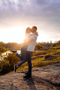 Romantik kaçamak, balayına romantik inişler, tek başına seyahat. Birbirlerine aşık çiftler doğada, gün batımında, sarı ve mor gökyüzü arka planında. Genç çift çayırda günbatımının tadını çıkarıyor..