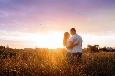 Romantik kaçamak, balayına romantik inişler, tek başına seyahat. Birbirlerine aşık çiftler doğada, gün batımında, sarı ve mor gökyüzü arka planında. Genç çift çayırda günbatımının tadını çıkarıyor..