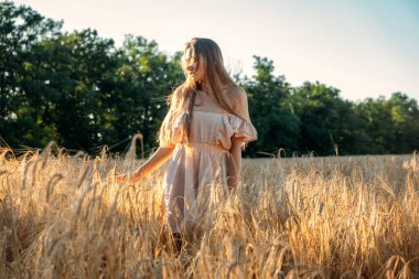 Doğa sağlığı faydaları. Doğayla bağlantı, dışarıda zaman, dışarıda izin günü. Doğa eksikliği bozukluğu. Gün batımında buğday tarlasında doğanın tadını çıkaran genç bir kadın..