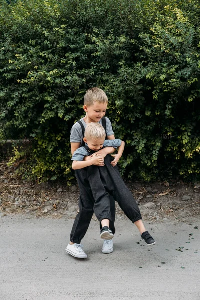 Dwoje braci bawi się razem w pobliżu domu. Dwóch małych chłopców przytula się bratersko i bawi na świeżym powietrzu. Wychowywanie rodzeństwa, które się dogaduje — Zdjęcie stockowe