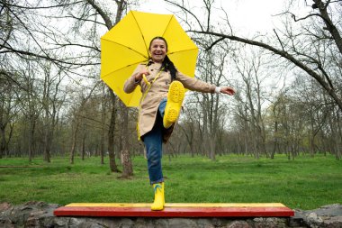 Mutlu yaşlı kadınlar dışarıda eğleniyor. Yaşlı, neşeli, olgun, yaşlı, sarı şemsiyeli emekli kadın yağmurlu bir parkta hayatın tadını çıkarıyor. Hayatın tadını çıkarmak, olumlu duygular, mutlu emeklilik.