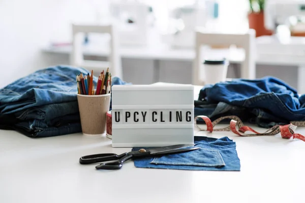Denim Upcycling Ideas, Using Old Jeans, Repurposing Jeans, Reusing Old Jeans, Upcycle Stuff. Lightbox dengan teks Upcycling, Stack jins biru tua, gunting, benang dan alat jahit di studio jahit. — Stok Foto