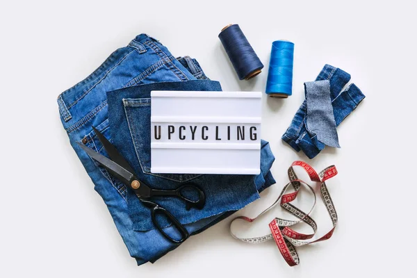 Denim Upcycling Ideas, Χρησιμοποιώντας παλιά τζιν, Repurposing Jeans, Επαναχρησιμοποίηση παλαιών τζιν, Upcycle Stuff. Lightbox με κείμενο Upcycling, Στοίβα από παλιά μπλε τζιν, ψαλίδι, κλωστή και ραπτομηχανές στο στούντιο. — Φωτογραφία Αρχείου