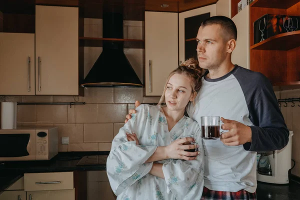 Pareja joven tomando café en la cocina en casa por la mañana. Joven pareja feliz, recién casados familia empezar un nuevo día y tomar café de la mañana juntos —  Fotos de Stock