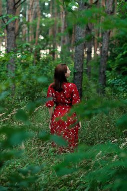 JOMO, kaçırmanın sevinci, doğayla bağlantı, zihinsel iyileşme, zihinsel sağlık, sakinlik konsepti. Kırmızı elbiseli ve hasır şapkalı genç kadın ormanda tek başına yürüyor.