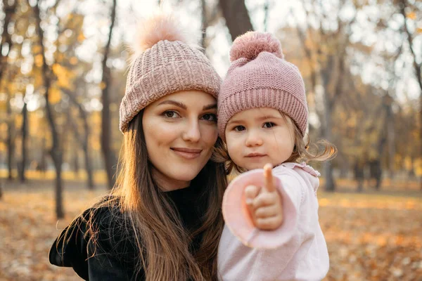 Ritratto ravvicinato di mamma e bambina nel parco autunnale con passeggino. Felice famiglia mamma e bambino all'aperto in autunno parco. Attività autunnali per bambini — Foto Stock