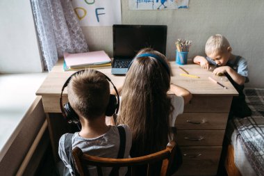 Evde dizüstü bilgisayarın yanında oturan kulaklık takan bir grup öğrenci ya da arkadaş. Aile, okul öğrencisi mesafesi öğrenme, video konferansında laptopta sanal sınıf, televizyon dersi..
