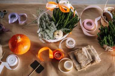 Overhead view of a Thanksgiving floral gift basket with heather, greenery, and ribbon surrounded by crafting supplies. Thanksgiving craft, seasonal floristry, handmade gifting, DIY workshop. High