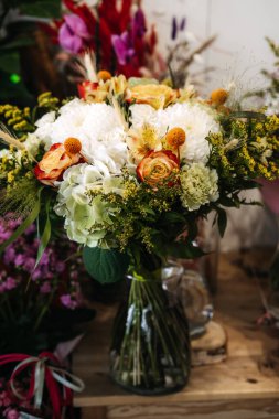 Autumn floral arrangement displayed in a clear glass vase on wooden surface. Seasonal bouquet design, cozy flower shop vibes, rustic natural decor, local florist craftsmanship. High quality photo
