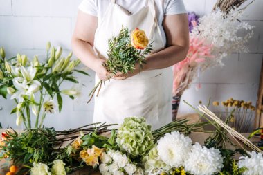 Sarı gül ve yeşillik desenli buketi mevsimlik çiçekçilik ortamında toplayan bir kadın. Dikkatli işçilik, yavaş çiçekçilik, buket yapım atölyesi, yaratıcı çiçek hobisi. Yüksek kalite fotoğraf