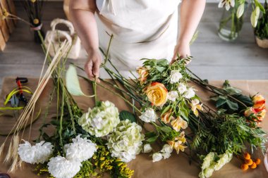 Sarı gül ve yeşillik desenli buketi mevsimlik çiçekçilik ortamında toplayan bir kadın. Dikkatli işçilik, yavaş çiçekçilik, buket yapım atölyesi, yaratıcı çiçek hobisi. Yüksek kalite fotoğraf
