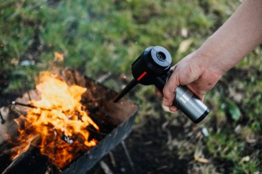 Metal bir yangını körüklemek için pille çalışan bir üfleyici kullanan bir elin yakın çekimi. Yangın başlatma teknolojisi, taşınabilir üfleyiciler, kamp aletleri, açık havada yenilik. Yüksek kalite fotoğraf