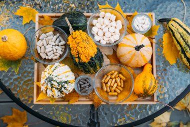 Rengarenk su kabakları ve cam kaselerde bulunan çeşitli takviyeler cam bir masanın üzerinde sarı yapraklarla ahşap bir tepside dizilmiş. Mevsimsel sağlık, bağışıklık artırma eğilimleri, fonksiyonel beslenme