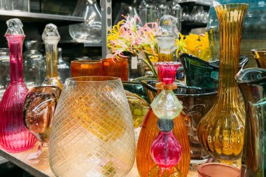 Vintage mağazasının raflarında renkli el yapımı cam eşyalar sergileniyor. Temalar arasında sanatta sürdürülebilirlik, iç dekorasyon eğilimleri, sanatsal tasarım, renk psikolojisi yer alıyor. Yüksek kalite fotoğraf