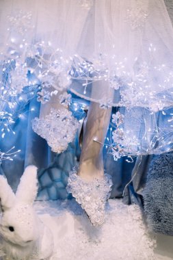 Kış temalı parlak ışıklar, sahte kar ve beyaz bir tavşanla kristal süslenmiş manken ayaklarının yakın çekimi. Fantezi perakende tasarımı, kış masalı, tuhaf tatil dekorasyonu..