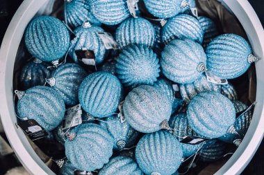 Perakende satış ortamında sergilenen açık mavi kurdeleli pırıltılı Noel mücevherleriyle dolu büyük bir kase. Tek renkli tatil, geleneksel olmayan dekorlar, mavi süsler. Varşova, Polonya, 20 Kasım 2024.