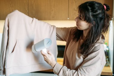 Kadın, mutfaktaki kazak için el yapımı buharlı giysi kullanıyor. Giysi ömrü uzatma, hassas kumaş bakımı, sürdürülebilir gardırop bakımı.
