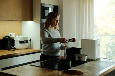 Kadın modern mutfakta yemek hazırlamak için hava kızartma makinesi kullanıyor. Bekar yaşam tarzı, bağımsız yaşam tarzı, tek kişilik yemek pişirme.