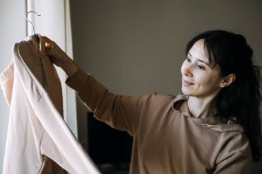 Kadın ikinci elbisesini giyerken askılı kapüşonluyu inceliyor. Sürdürülebilir moda, bilinçli tüketim, kostüm organizasyonu