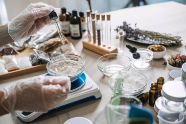 Eldivendeki eller, dijital ölçekte bir kase toza sıvı eklemek için cam damlatıcı kullanır. Phytokimya, bitki bazlı aktif bileşenler, botanik araştırması, laboratuvar hassasiyeti