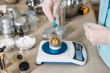 Eldivenli ellerin cam kaplara dijital ölçekte çiçek yaprakları yerleştirdiği yüksek açılı görüntü. Yeşil kimya, güzellik biyoteknolojisi, sürdürülebilir laboratuvar uygulamaları, botanik yeniliği