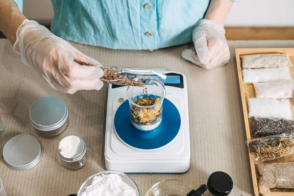 Eldivendeki eller kahverengi tohumları cam şişeye döküyor. Dijital ölçekte, ahşap tepsinin yanında, kesesi olan. Kozmetik formülasyonu, aktif bileşenler, eczacılık atölyesi, botanik bilimi