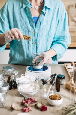 Koruyucu eldivenler giyen biri dijital ölçekte cam şişeye botanik malzemeler ekler. Mikro-imalat, zanaat laboratuvarı, küçük ölçekli kozmetik ürünler.