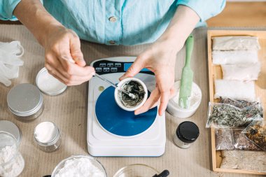 Eller elektronik ölçekte, kavanozlar ve organik malzemelerle çevrili küçük bir kasede botanik karışımı karıştırır. Zehirli olmayan bileşenler, organik cilt bileşenleri, kimyasal olmayan güzellik, botanik özleri.