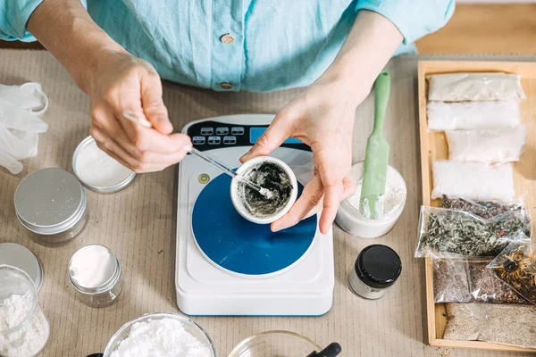 Eller elektronik ölçekte, kavanozlar ve organik malzemelerle çevrili küçük bir kasede botanik karışımı karıştırır. Zehirli olmayan bileşenler, organik cilt bileşenleri, kimyasal olmayan güzellik, botanik özleri.