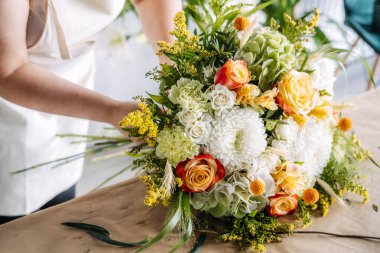Çiçekçi, çeşitli botanik saplarıyla kaplı kağıt üzerine karmaşık buket düzenler. Çiçek eğitimi, buket yapım dersi, botanik sanat atölyesi.