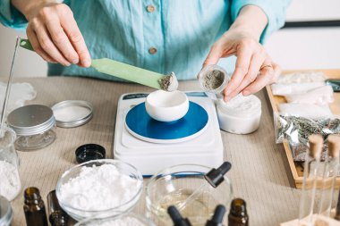 Eller, küçük kavanozdan kaseye elektronik ölçekte gri tozu ölçmek için yeşil spatula kullanır. Bitki egzozları, biyo-sinyal iletimi, cilt yenileme, hücresel iletişim