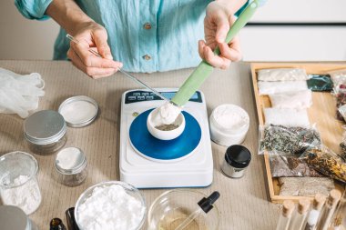 Eller dijital ölçekte beyaz tozu kaseye ölçmek için spatula ve cam çubuk kullanır. Mikrobiyom cilt bakımı, Probiyotik Güzellik, Postbiyotik Maskeler