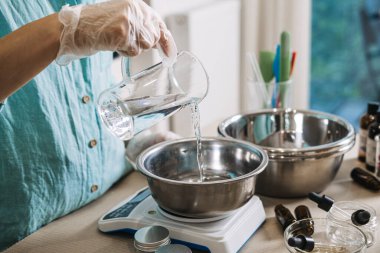 Dijital ölçekte insan cam sürahiden metal kaseye sıvı döker. Kozmetik emülsiyon fiziği, yağ ve suyu karıştırma estetik, cilt bakımı bilimi, profesyonel krem üretimi